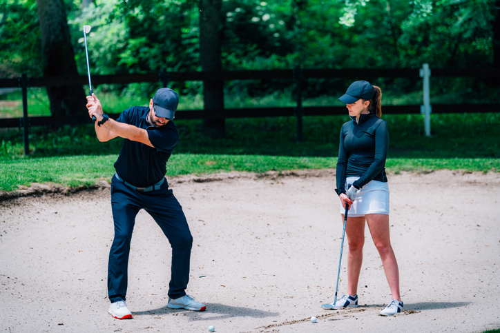 Golf sand bunker playing technique. Young woman practicing bunker shots with golf instructor
