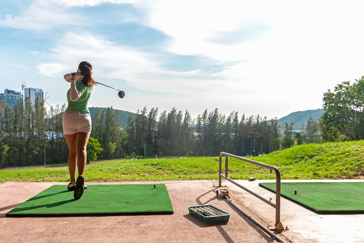 Healthy Sport. Asian sporty woman swing golf ball practice at golf driving range on evening on time for healthy sport. Lifestyle and Sport Concept