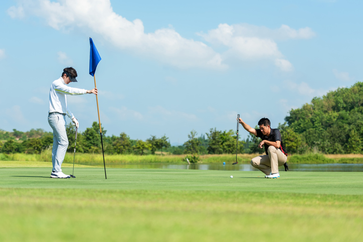 Golfer man and friend playing golf aiming shot for putting ball on the hole with club on green course. Professional people hobby in holiday and vacations in sunny morning day on club golf. Lifestyle and Sport Concept