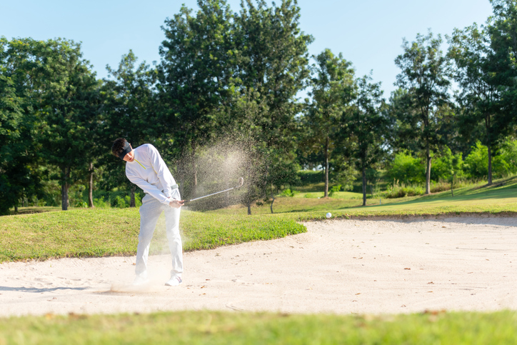 Asia Golfer man hitting out of a sand trap. The golf course is on the sand. Hobby in holiday and vacations on club golf. Lifestyle and Sport Concept