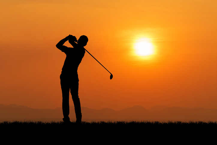 Golfer silhouetted against orange sunset