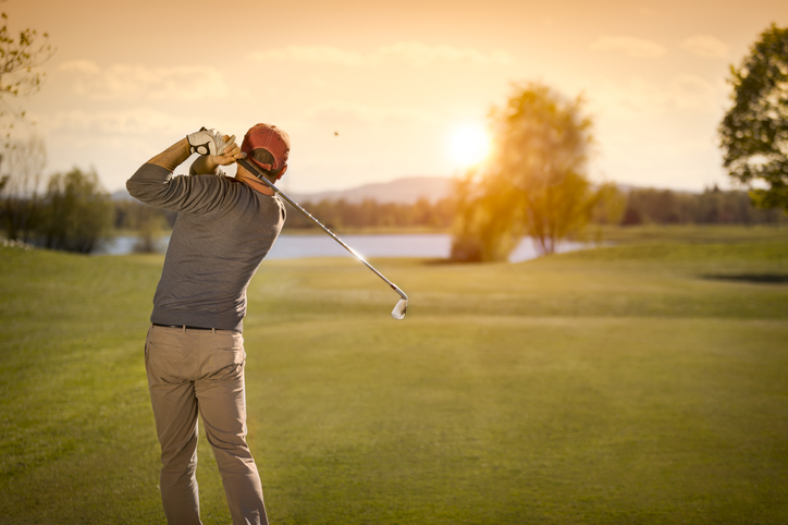 Male golf player swinging golf club at dusk.