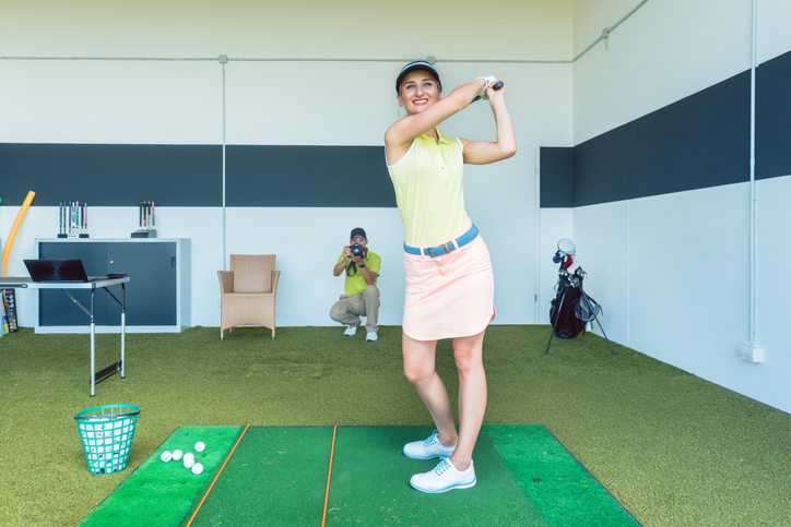 fit woman practicing golf swing during professional class indoors