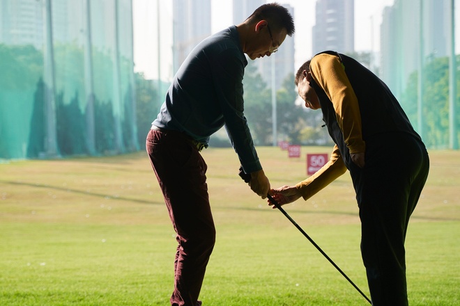 rear view of coach teaching Asian man practicing golf swing
